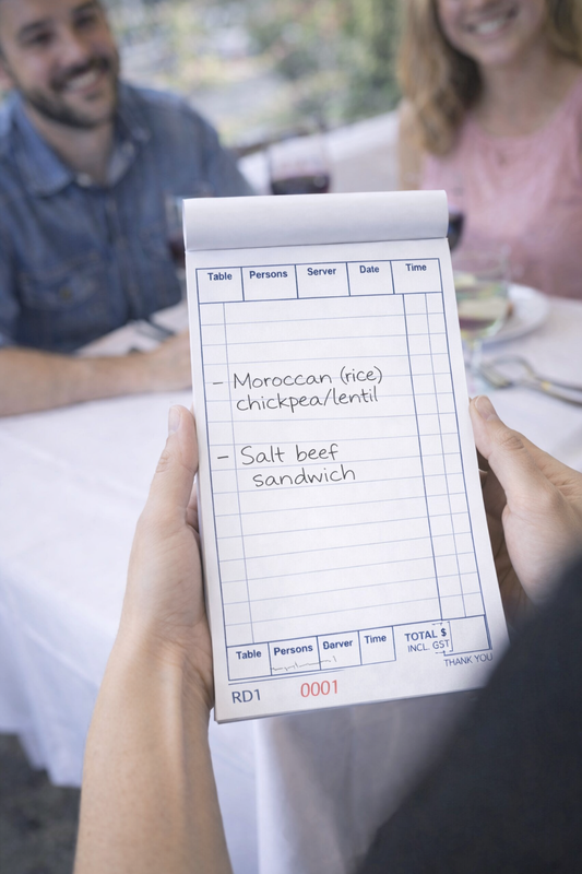 Person holding a restaurant order pad with a menu item list at a table.