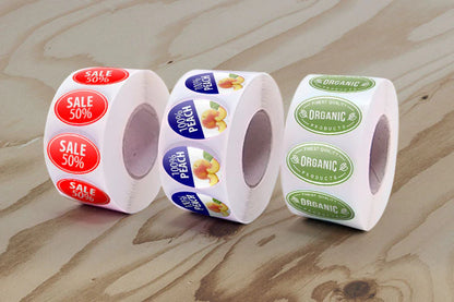 Three rolls of stickers on a wooden surface, including sale, peach, and organic labels.